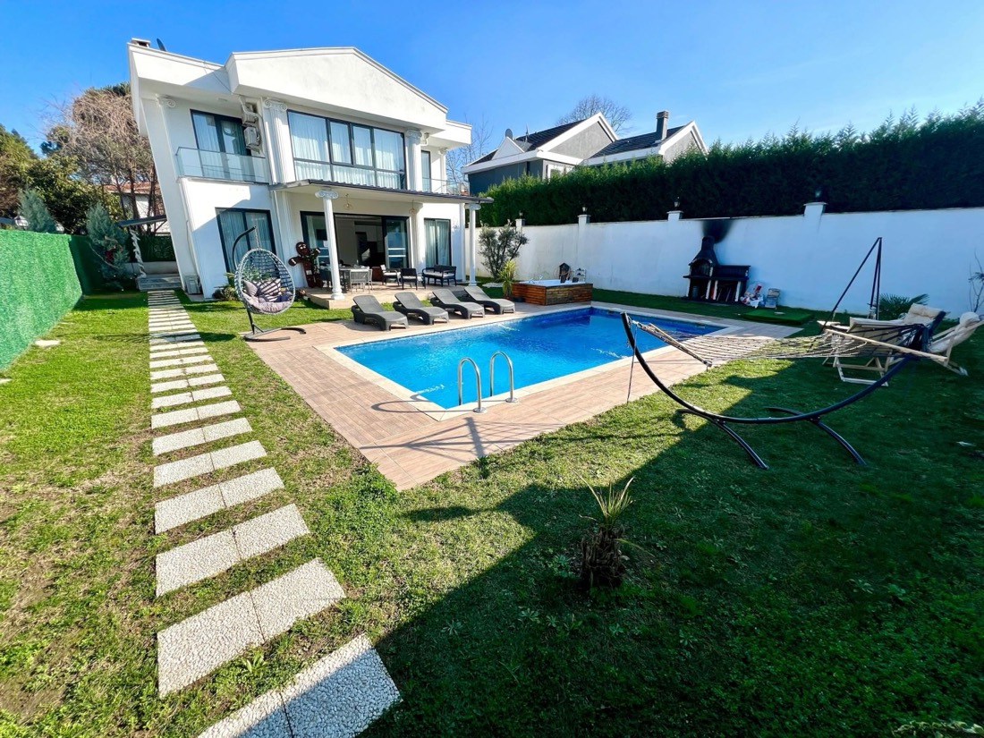 Güneşli bir günde villa, mavi havuz, şezlonglar ve geniş çim bahçe